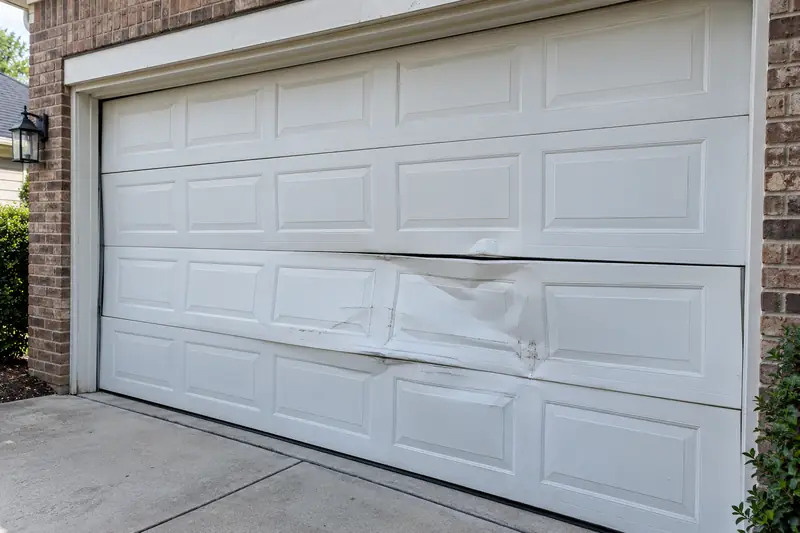 White two-car steel garage door with the third panel creased and buckled across the middle